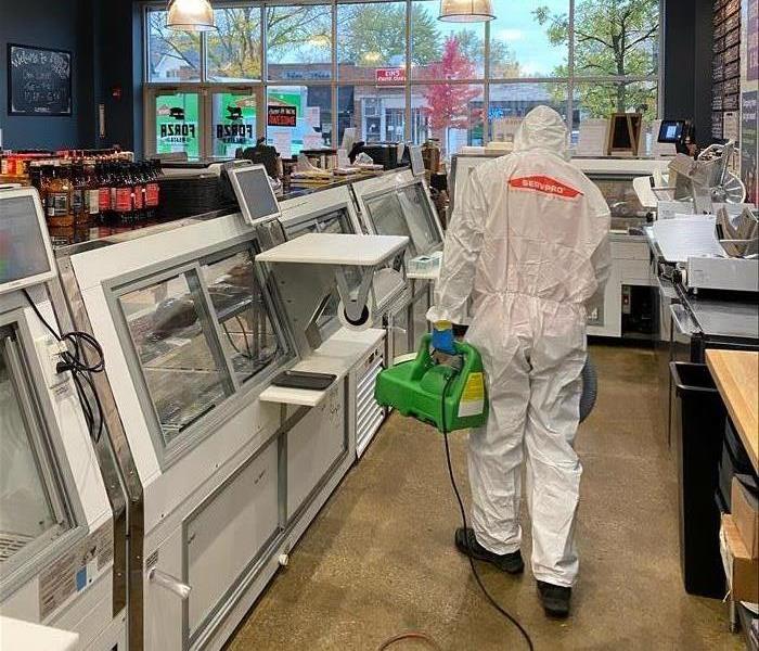 Tech suited up in PPE applies disinfectant inside a butcher shop